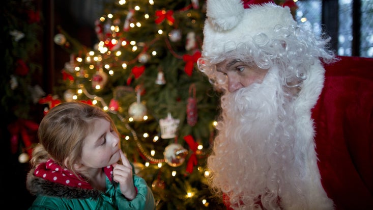Small girl talking to Father Christmas with brightly lit Christmas tree in background